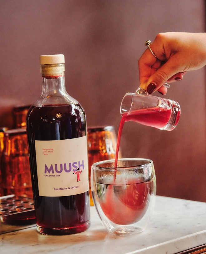 bottle of raspberry lychee drink next to a glass of the pink bevarage