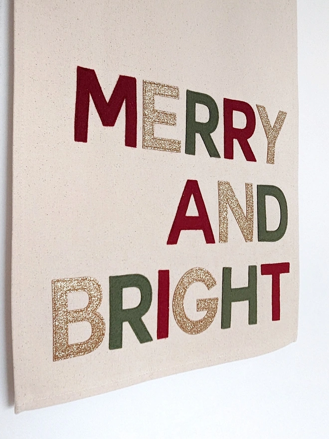 Close up of a fabric Christmas banner with Merry and Bright stitched in traditional Christmas colours