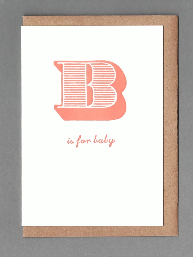 White card with orange text reading 'B is for baby' with a kraft envelope behind it