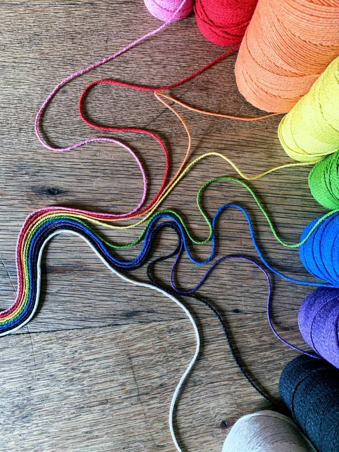 Cotton string in many colours pulled from the spools to form a rainbow on an oak table