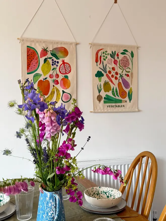 Fruit Print Fabric Banner, hanging on a white wall, next to a set table with flowers. 