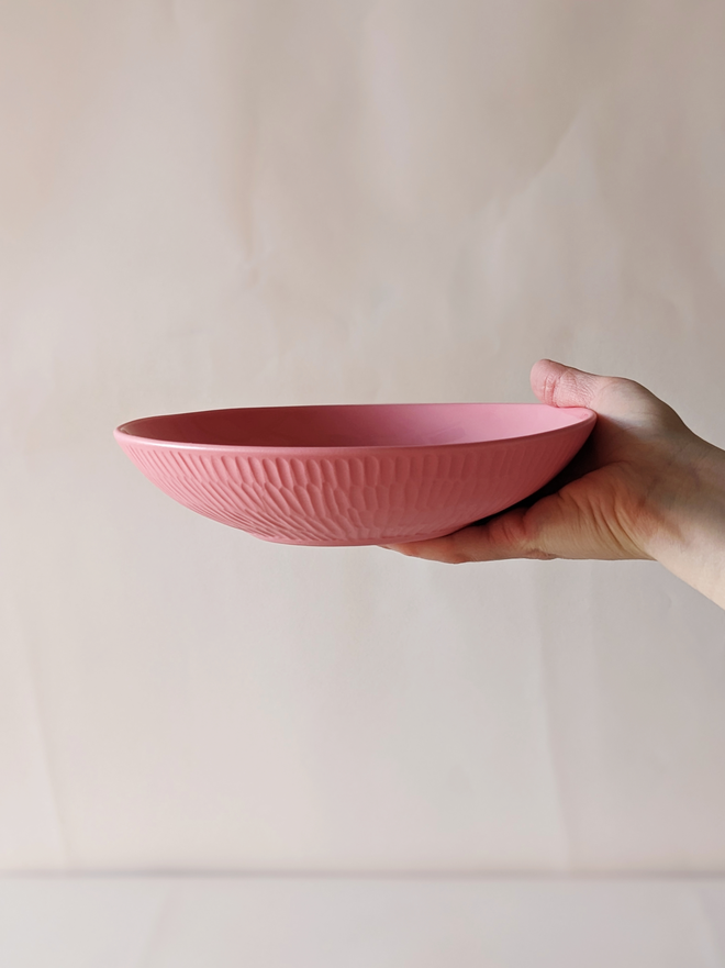 Porcelain Pasta Bowl in Milkshake Pink with hand carved scalloped details being held in a hand  