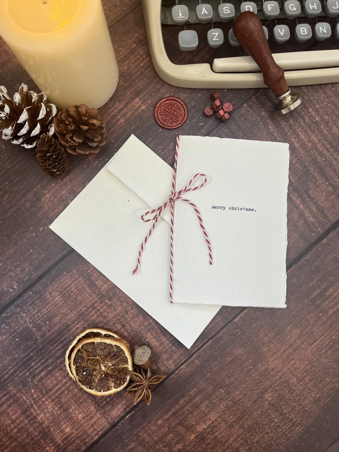 handmade a6 christmas card typewritten with an antique typewriter with the words merry christmas onto cotton rag deckle paper. with a matching c6 cotton rag envelope and a red christmas wax seal stamp and candy cane red and white stripe twine string