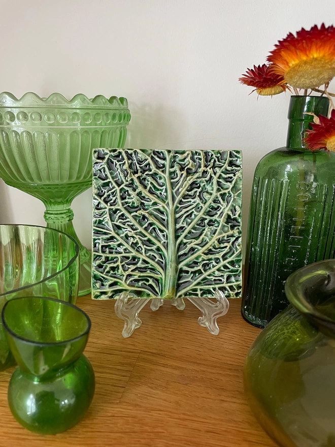 Decorative eye-catching savoy cabbage feature tile – three-dimensional, very realistic and incredibly tactile - displayed on a mantelpiece alongside antique green glass. 