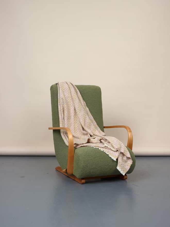 cairmeal lambswool blanket. a pink and brown blanket thrown over a green chair.
