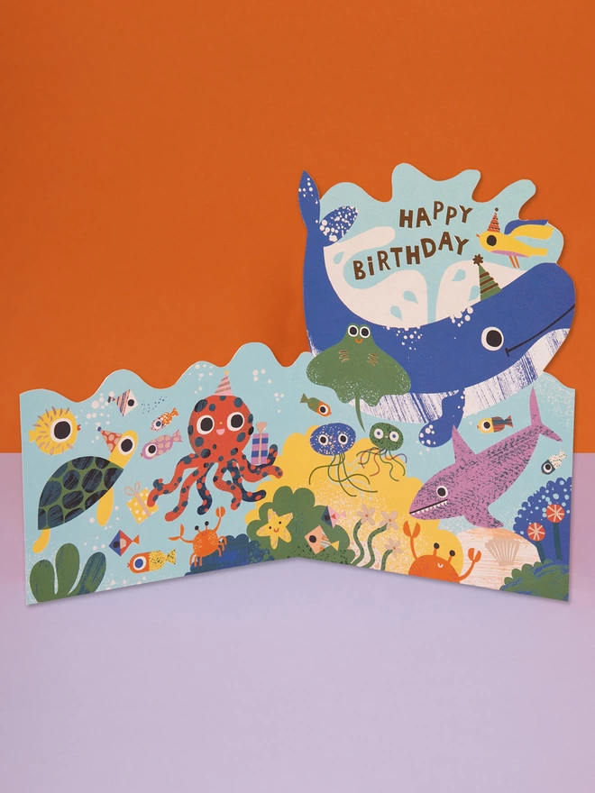 An under the sea themed die cut Birthday card filled with colourful characters in party hats such as a turtle, jellyfish, octopus and even a whale. The card is complete with gold foil details and a gold foil ‘Happy Birthday’ message