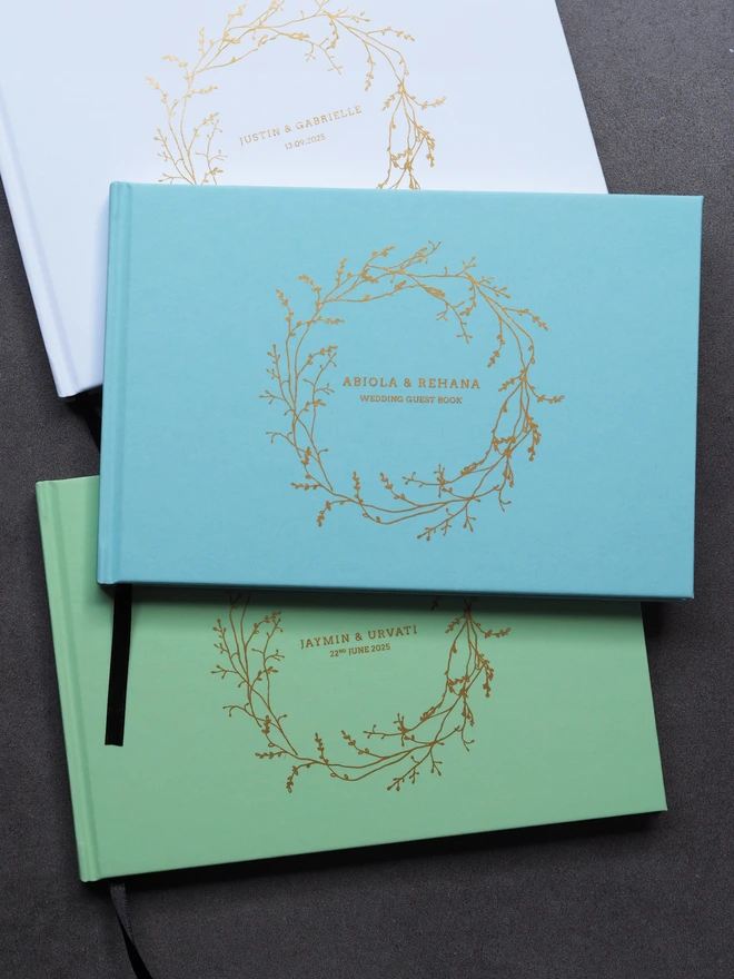 Personalised Wedding Guestbook. A personalised hardcover wedding guestbook with a delicate gold vine wreath illustration on the front and personalise with names and a date. 