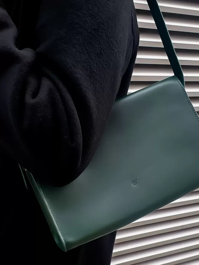 Dark Green Handbag Worn Under Shoulder on a Dark Wool Jacket. There is a Steel Shutter in the background