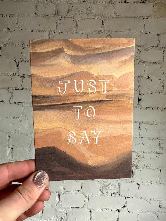a greetings card featuring an illustration of a sand dunes landscape with the text “just to say”