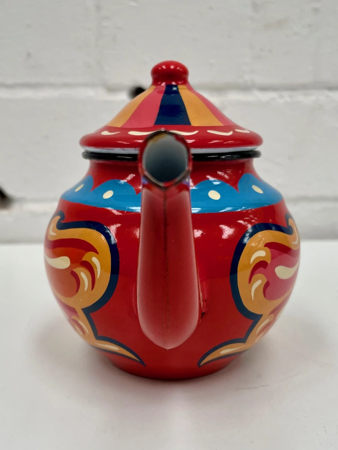 Small red vintage enamel teapot, hand painted with a traditional fairground inspired design in pink, orange and yellow. Teapot has a hinged lid.