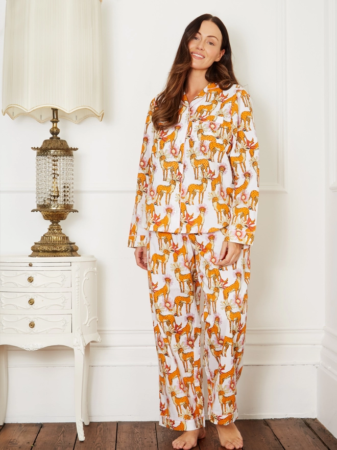 Model stands smiling and tilting her head while wearing full length traditional pyjamas with a button through shirt and wide legged trousers