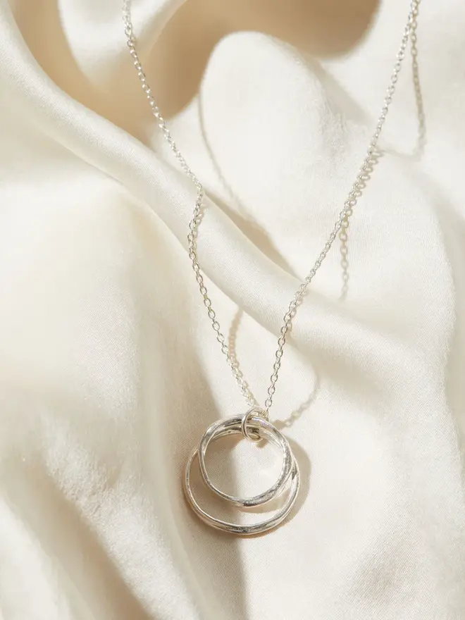 Sterling Silver Double Circle 'You and Me' Necklace draped over a silk material