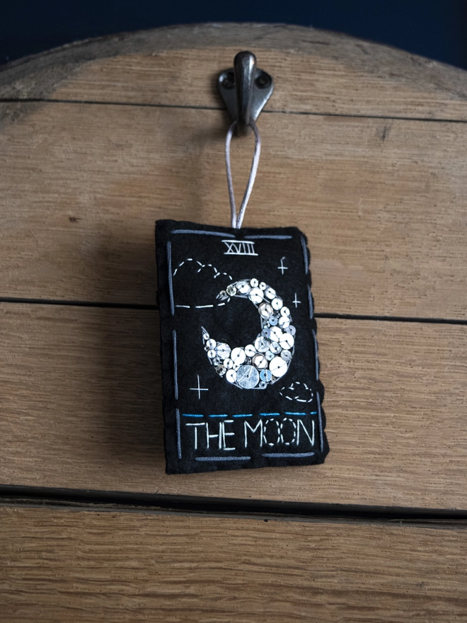 A handcrafted felt ornament with sequins and embroidery depicting "The Moon" tarot card. 