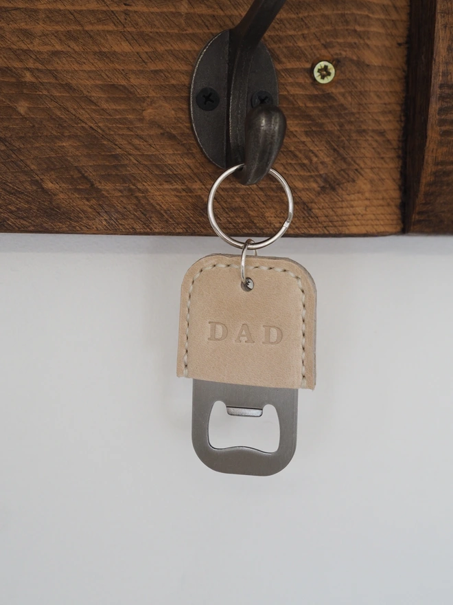 Handmade personalised leather bottle opener key ring. A leather key ring in natural cream, stamped with the name DAD.