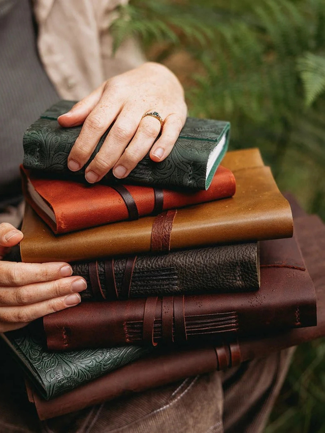 make your own leather journal. a stack of brown and green leather journals.