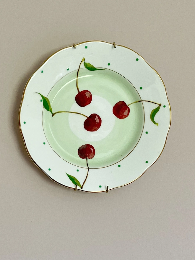 cherries painted on a pale green plate with polka dotted details