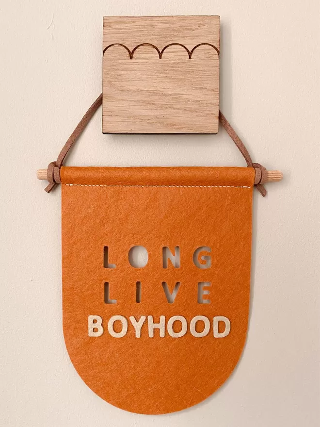 Orange flag saying long live boyhood hanging by a wooden hook.