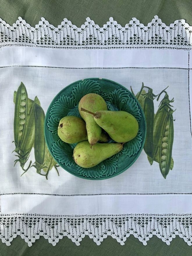 A beautiful vintage cotton cloth with drawn thread work and deep lace edges, overprinted with green pod peas and  shown with a majolica plate of pears