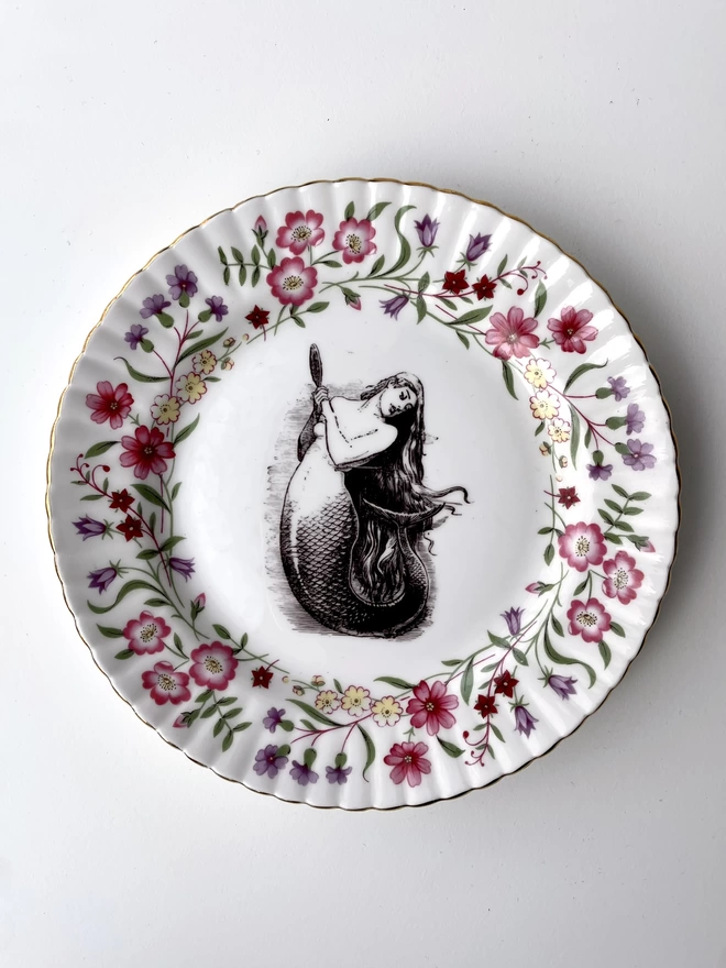 vintage plate with an ornate border, with a printed vintage illustration of mermaid in the middle 