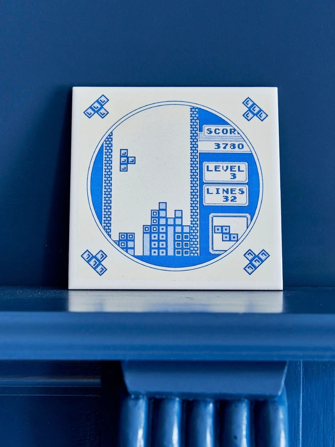 Hand Printed Delft Style Tetris Tile by Haus of Lucy seen in front of books.