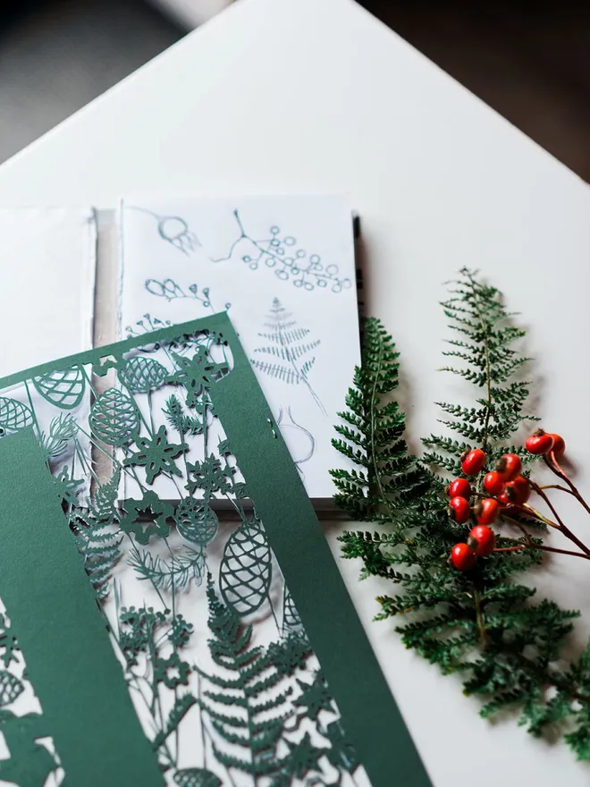 Work in progress, Letter D botanical papercut initial D in dark green shown with sketchbook and winter foliage