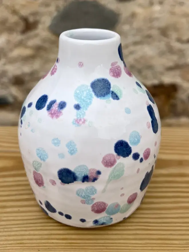 Sweetpea Bud Vase, a colourful vase sitting on a wooden surface against a brick wall backdrop.