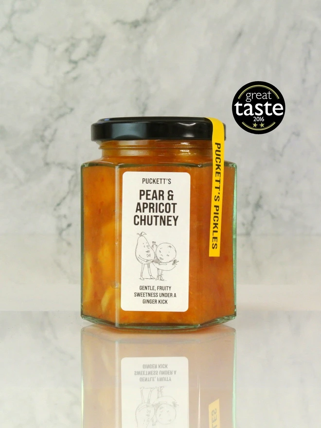 pear and apricot chutney. a jar of pear and apricot chutney photographed against a marble background.