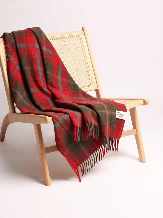 Dark Maple Tartan Blanket, a red blanket draped over a wooden chair on a white surface against a plain backdrop. 