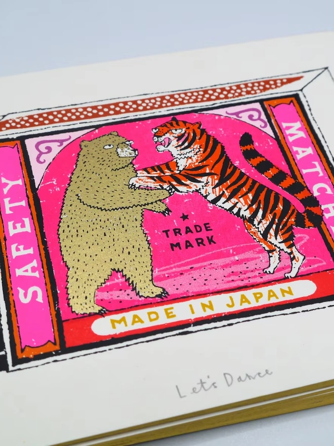 Bear And Tiger Matchbox Let's Dance, a colourful matchbox design on a white screenprint. It sits against a baby blue backdrop. 