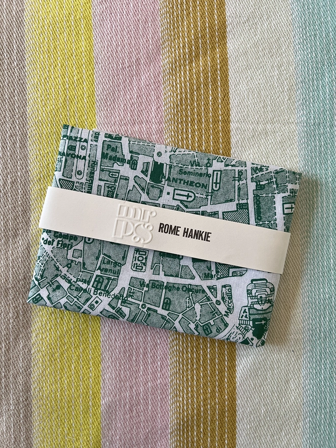 A Mr.PS Rome map handkerchief, folded and packaged, on a stripy tablecloth