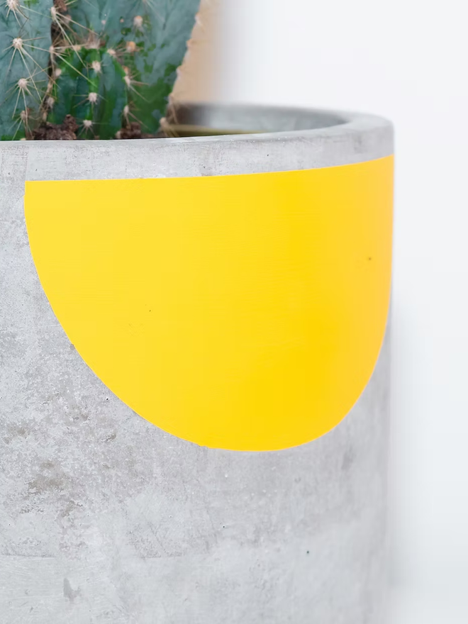 sunny concrete plant pot. a grey plant pot with a yellow half sun pattern painted around the top rim.