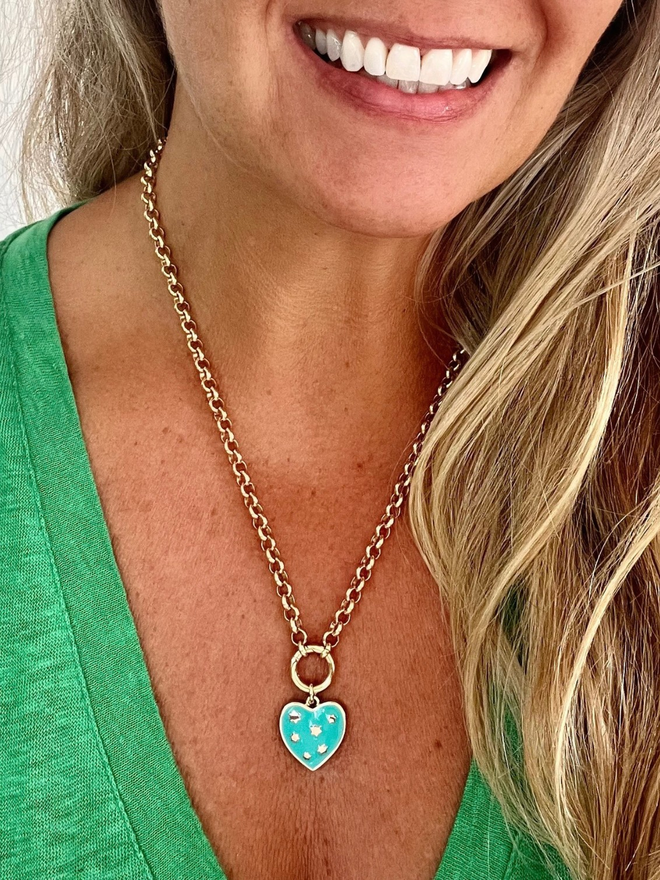 Woman in green t shirt wearing gold chain necklace with hanging turquoise heart charm