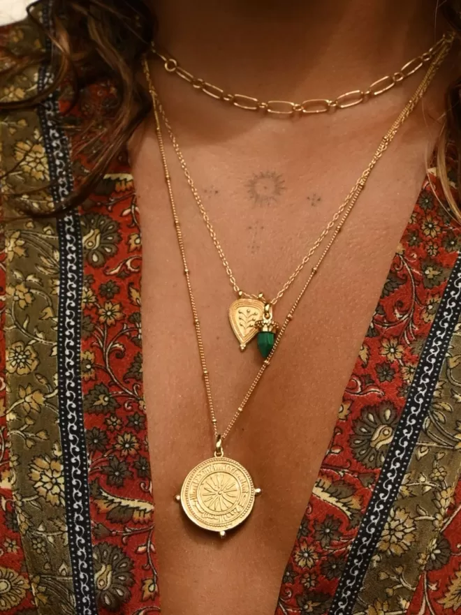 Model wearing gold boho layering necklaces with long coin compass pendant and smaller leaf pendant with green malachite charm 