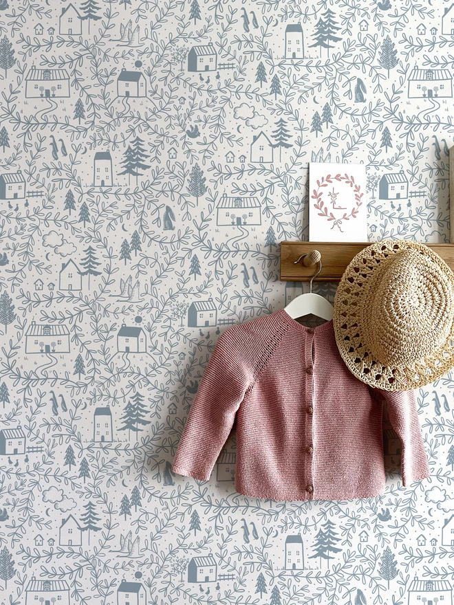 Cottages in the woods dusk blue wallpaper in girls nursery with hooks, hat and pink cardigan