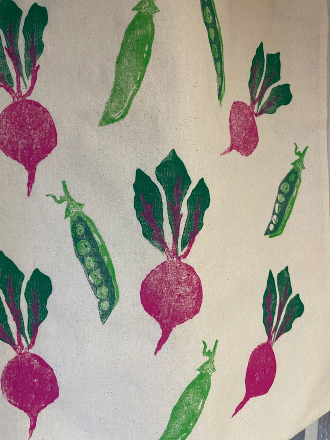 Beetroot And Pea Kitchen Tea Towel. White fabric with a diagonal pattern of green pea pods and beetroots, some open to show bright green peas.