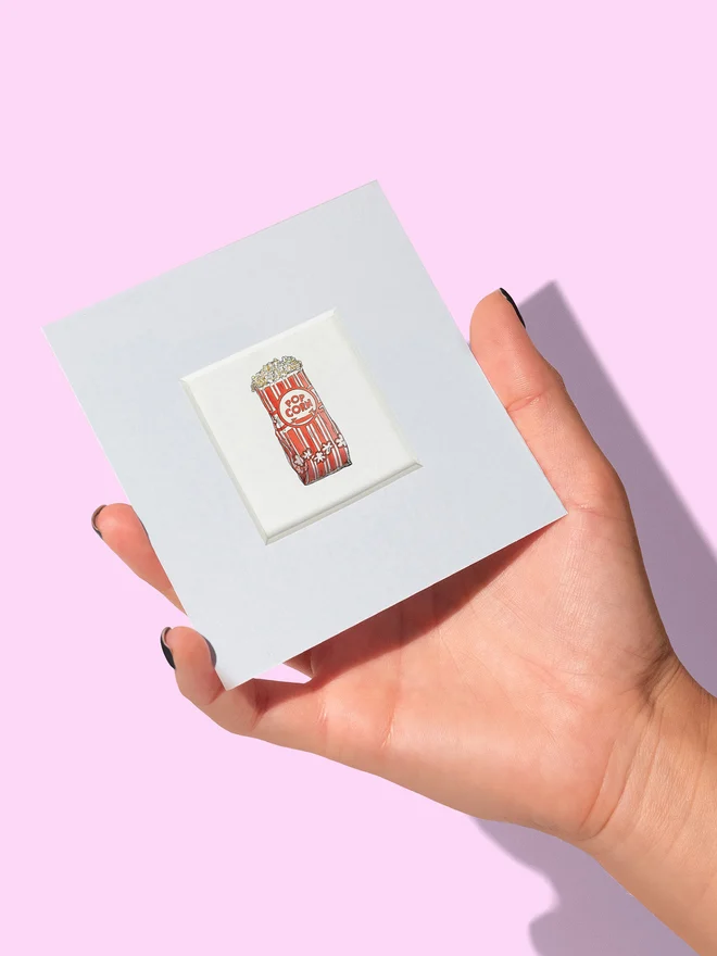 Hand holding a mini popcorn print showing the actual size of the tiny print