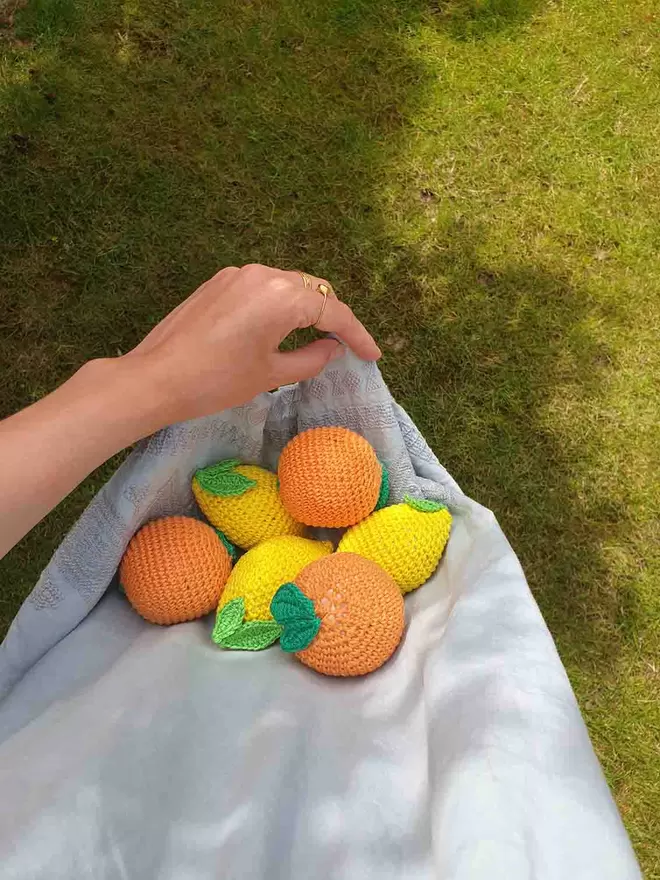 Three crochet lemons and oranges carried in light blue fabric.
