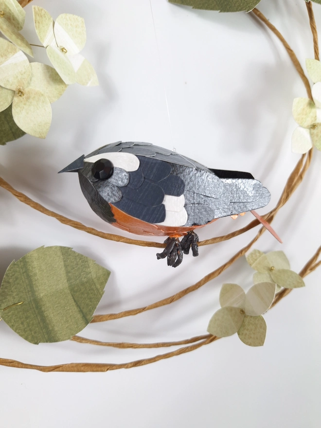 handmade paper sculpture of a redstart bird, perched on a wreath of green hydrangea blooms