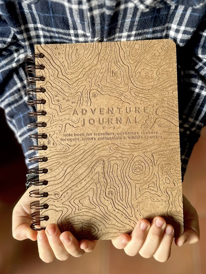 Wooden Hardback Adventure Journal, a person holding an adventure journal in their hands above a brown floor. 