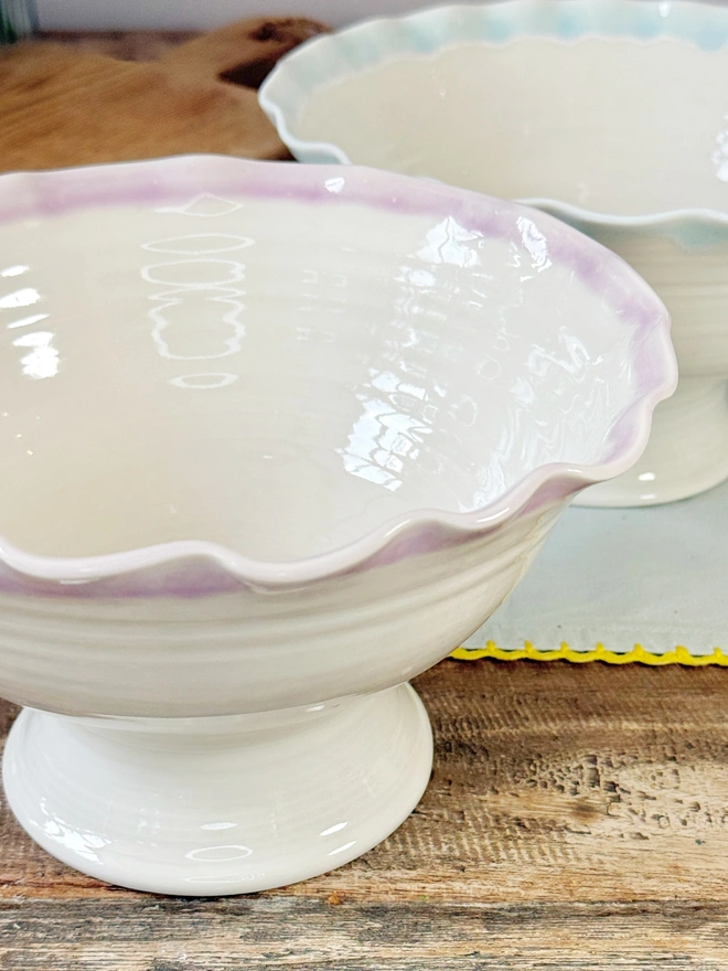 Undulating hand thrown porcelain stem bowls with satin cream glaze and pink or turquoise rim on a rustic table top