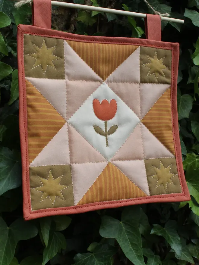 tulip quilt wall hanging. a patchwork quilt with a pink star pattern in the centre and embroidered tulip.