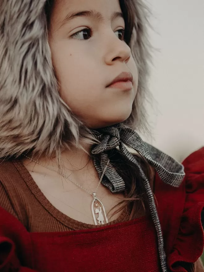 Profile of child wearing fur bonnet and silver chain with silver and gold pendant