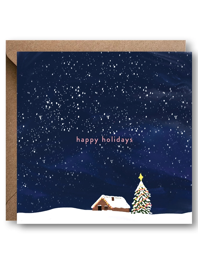 Christmas card with a snowy cabin and christmas tree against a night sky. Message reads happy holidays