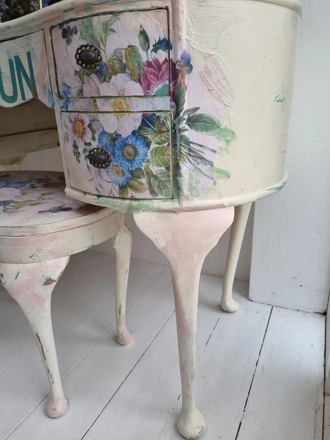 A painted dressing table in white and pale pink with large florals in blues and mauves and text in turquoise that reads 'turn your face to the sun'. The whole piece is distressed in the shabby chic style.