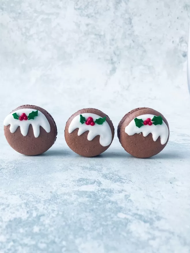 three macarons decorated like Christmas puddings with little holly leaves & berries