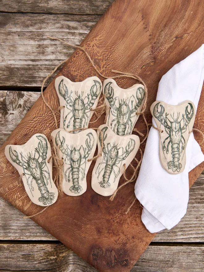 Ceramic Lobster Napkin Ring Holder, a ceramic lobster napkin sitting on a wooden chopping board. 