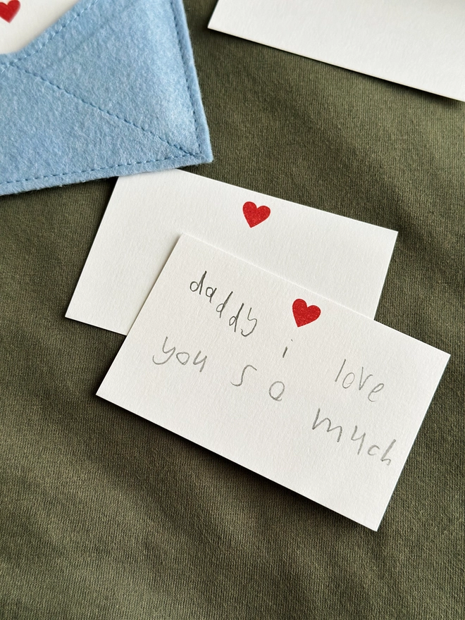 Two handwritten notecards lay beside a handmade felt envelope, each with a sweet note to Daddy from children.