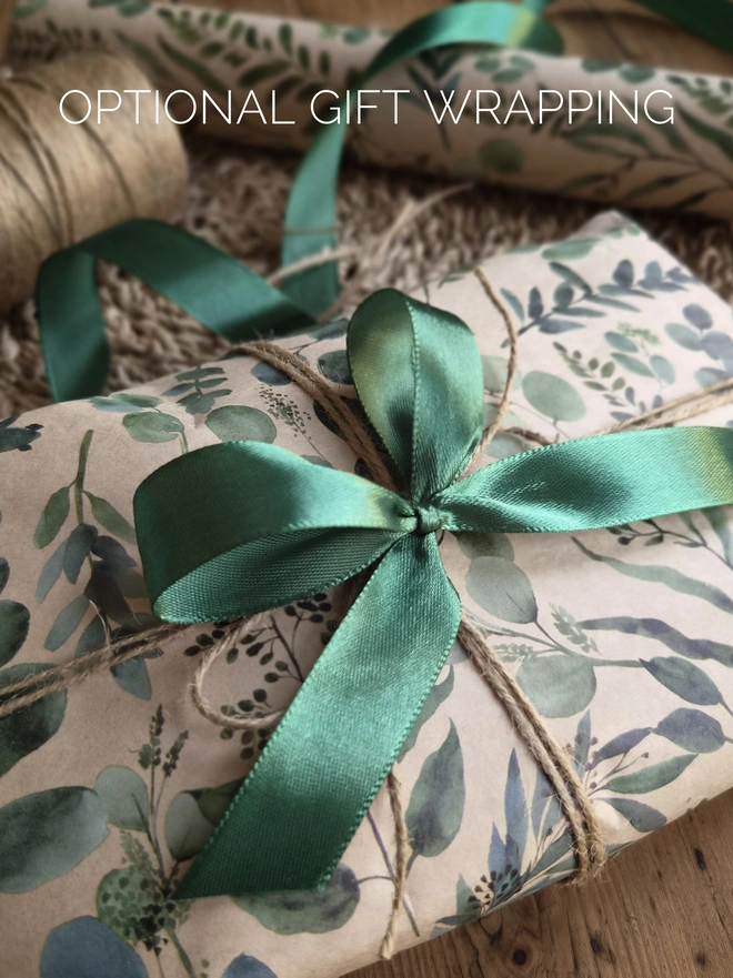 A gift wrapped in kraft paper with a green Eucalyptus leaf print. Finished with twine and a green bow.