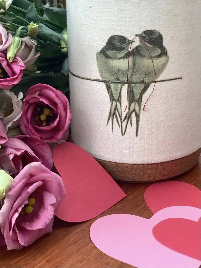 a tealight candle holder featuring birds on a line with a red thread in their beaks