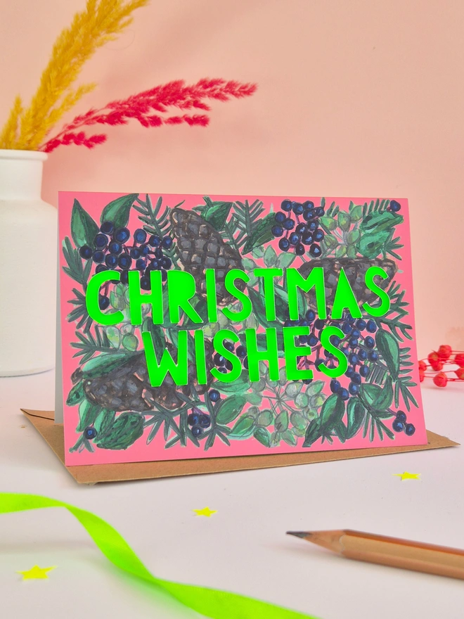Pine Cone and blue berry illustration card with Christmas Wishes in paper cut text and a neon green backing paper 